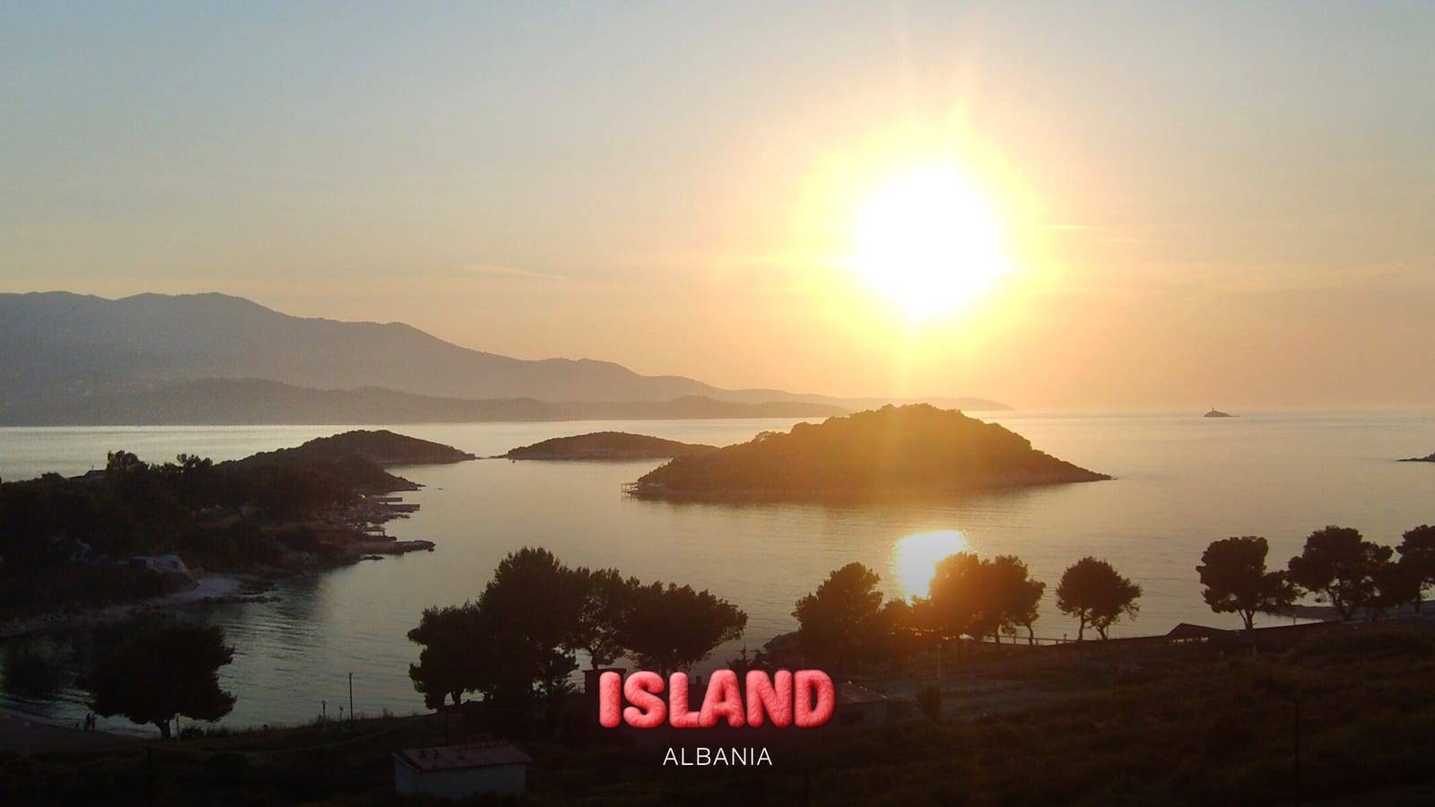 The islets of Ksamil at sunset seen from the hillside, with the sun reflected in the bay, Albania, with the Party Island Albania logo